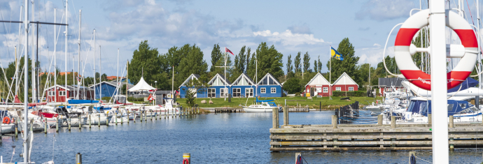 Indsejling til lystbådehavnen. Både der ligger til kaj. Bagerst rødt hus der huser havnekontoret og et blåt hus der huser sejlklubben.