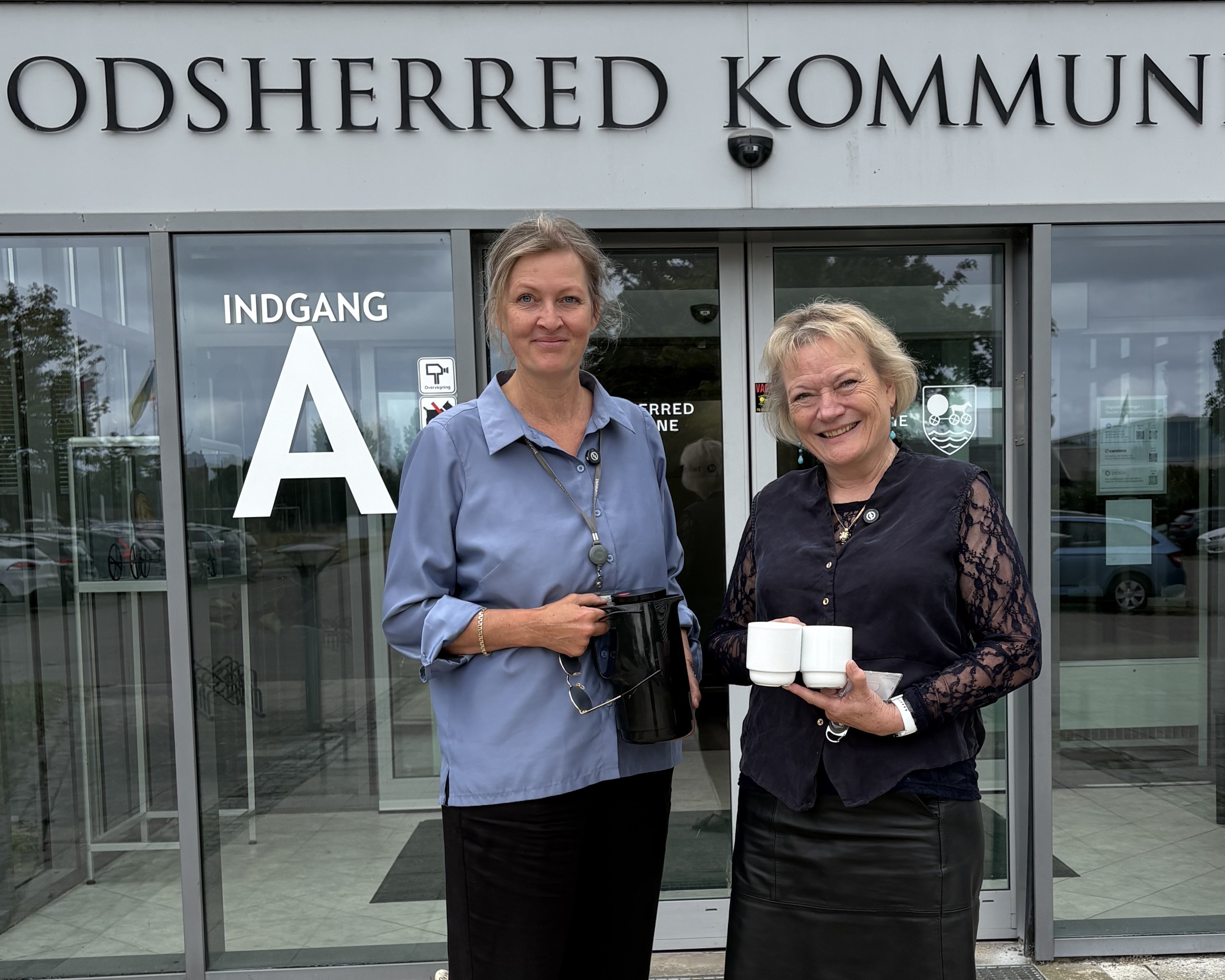 Kommunaldirektør Mette Touborg og borgmester Hanne Pigonska foran rådhuset med en termokande og to kopper